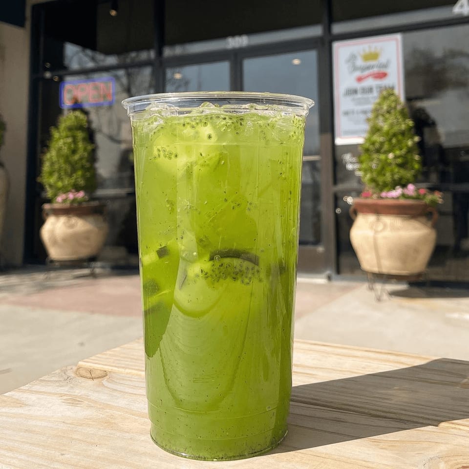 Green drink with kiwi slices and chia seeds on a wooden table outside a restaurant.