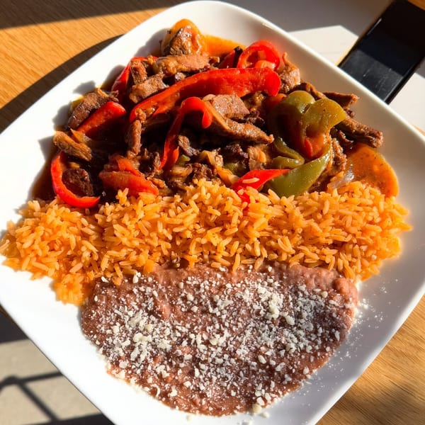 Beef fajitas with red and green peppers, rice, and refried beans on a white plate.