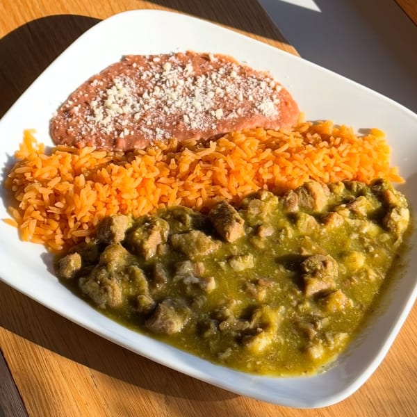 Pork chile verde with orange rice and refried beans topped with cheese on a white plate.