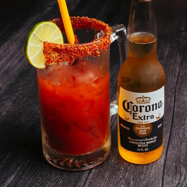 A michelada in a mug with a lime and a Corona Extra beer bottle on a dark wooden surface.