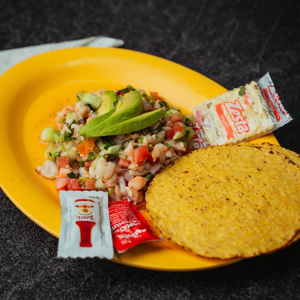 Shrimp ceviche with avocado, tomatoes, and cucumbers, served with tostadas and crackers on a yellow plate.