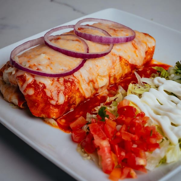 A cheesy burrito covered in red sauce and red onion rings, served with pico de gallo and sour cream.